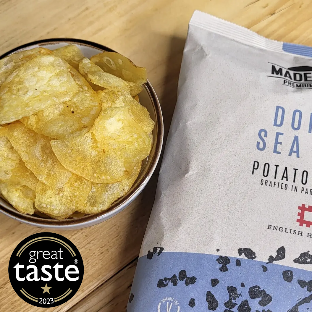 A birds eye view of a bowl of Made For Drink's Dorset Sea Salt crisps with an unopened packet laying by the side. A 1 gold star Great Taste 2023 logo is showing in the foreground.