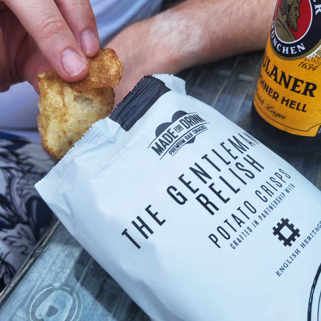 A hand reaching into a 40g pack of Made For Drink's The Gentleman's Relish potato crisps.