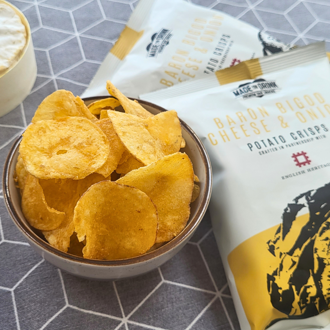 A bowl full of Made For Drink's Baron Bigod Cheese & Onion crisps with 2 unopened 40g packets laying down next to it in the background.