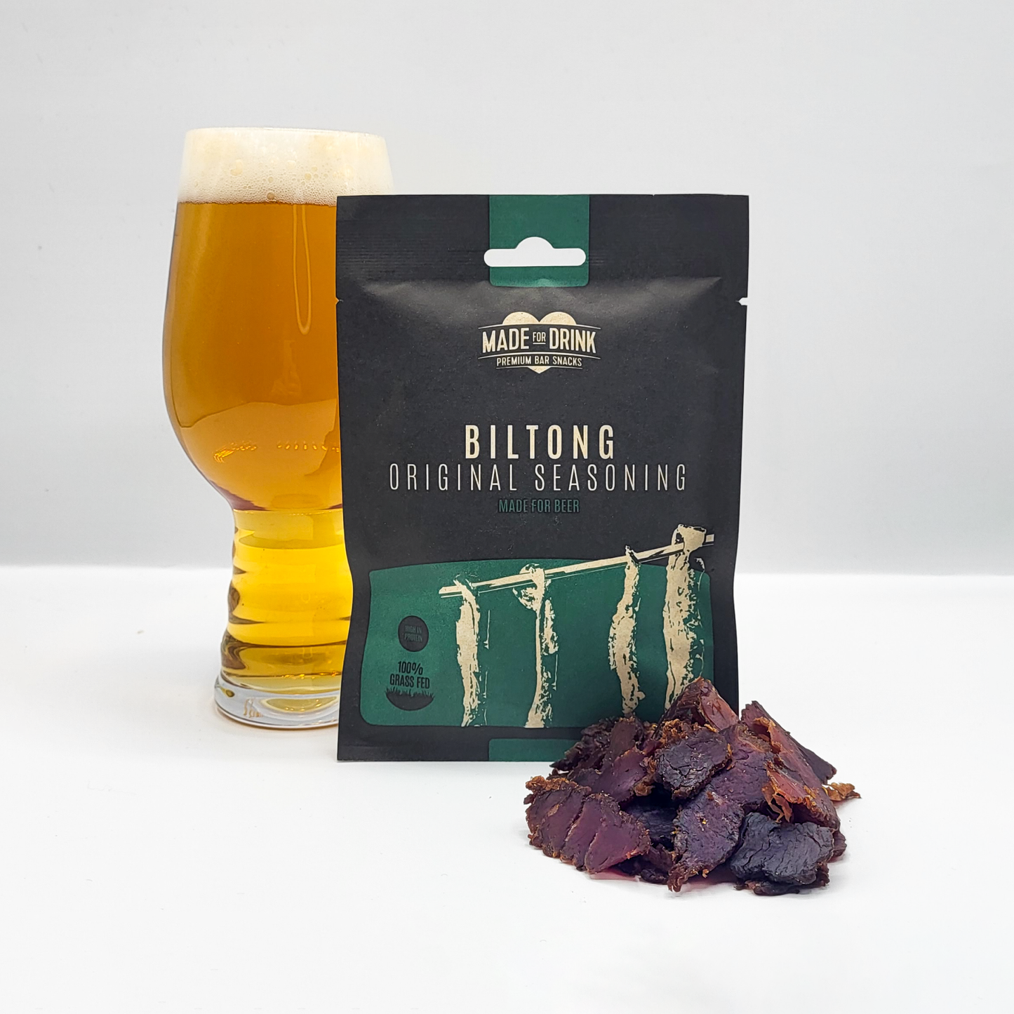 A 30g pack of Made For Drink's 100% Irish Grass-Fed Beef Biltong standing in front of a pint of lager with a small pile of biltong in the foreground.