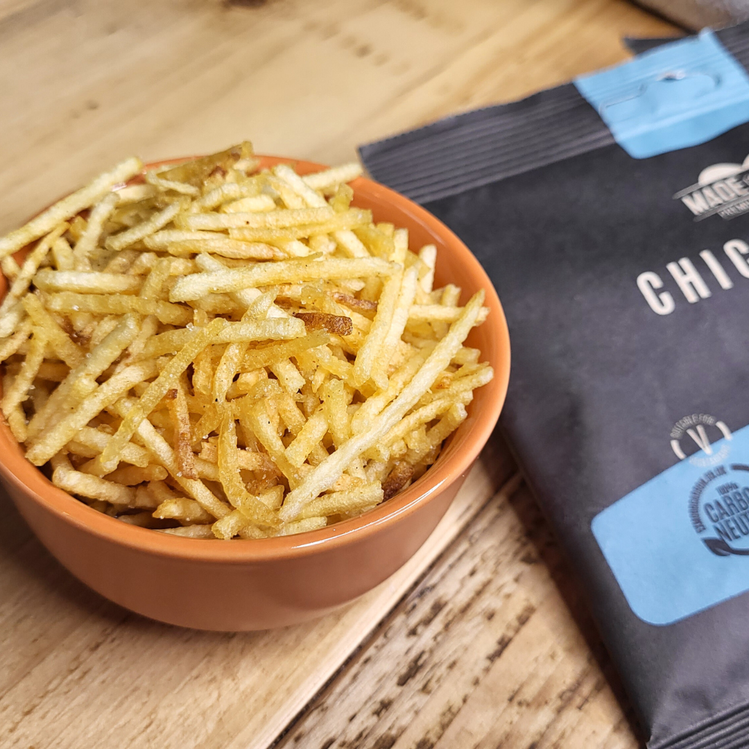 A bowl of Made For Drink's Chicken Salt Fries with a 40g pack lying on a wooden table in the background.