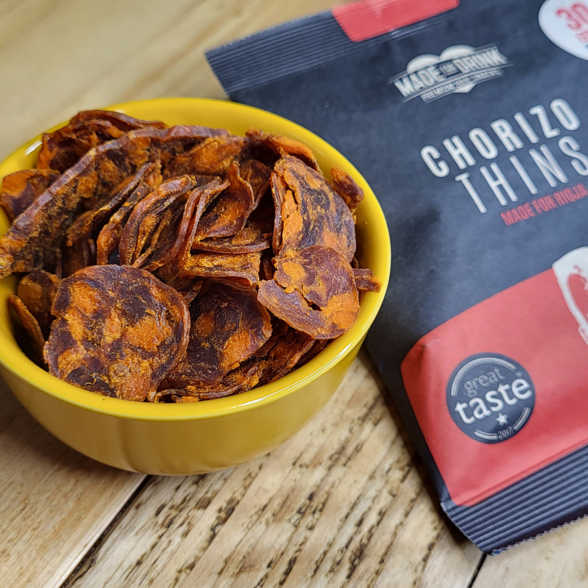 A bowl of Made For Drink's Chorizo Thins with a pack laying on the table by the side