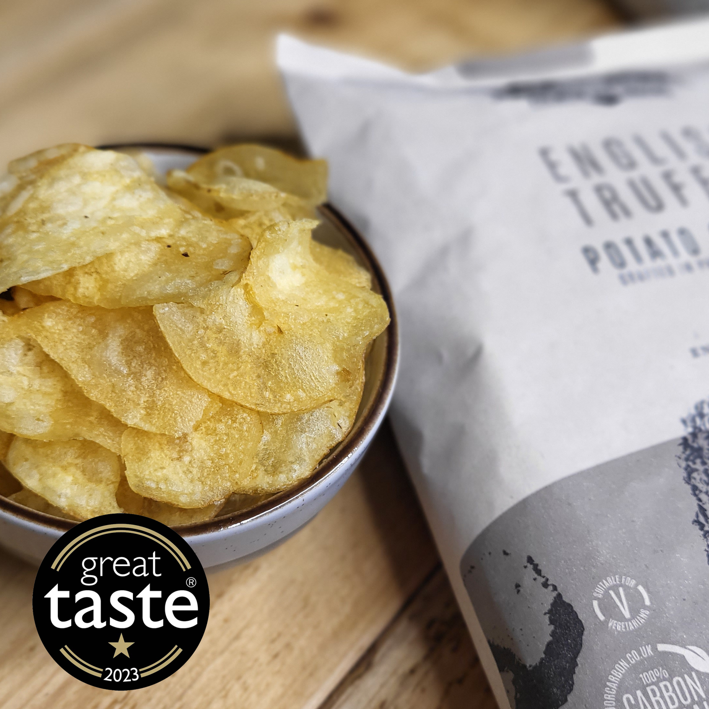 A bowl of Made For Drink's English Truffle crisps on a wooden table with an opened pack partially visible in the background. A one gold star Great Taste 2023 Logo is sowing in the foreground.