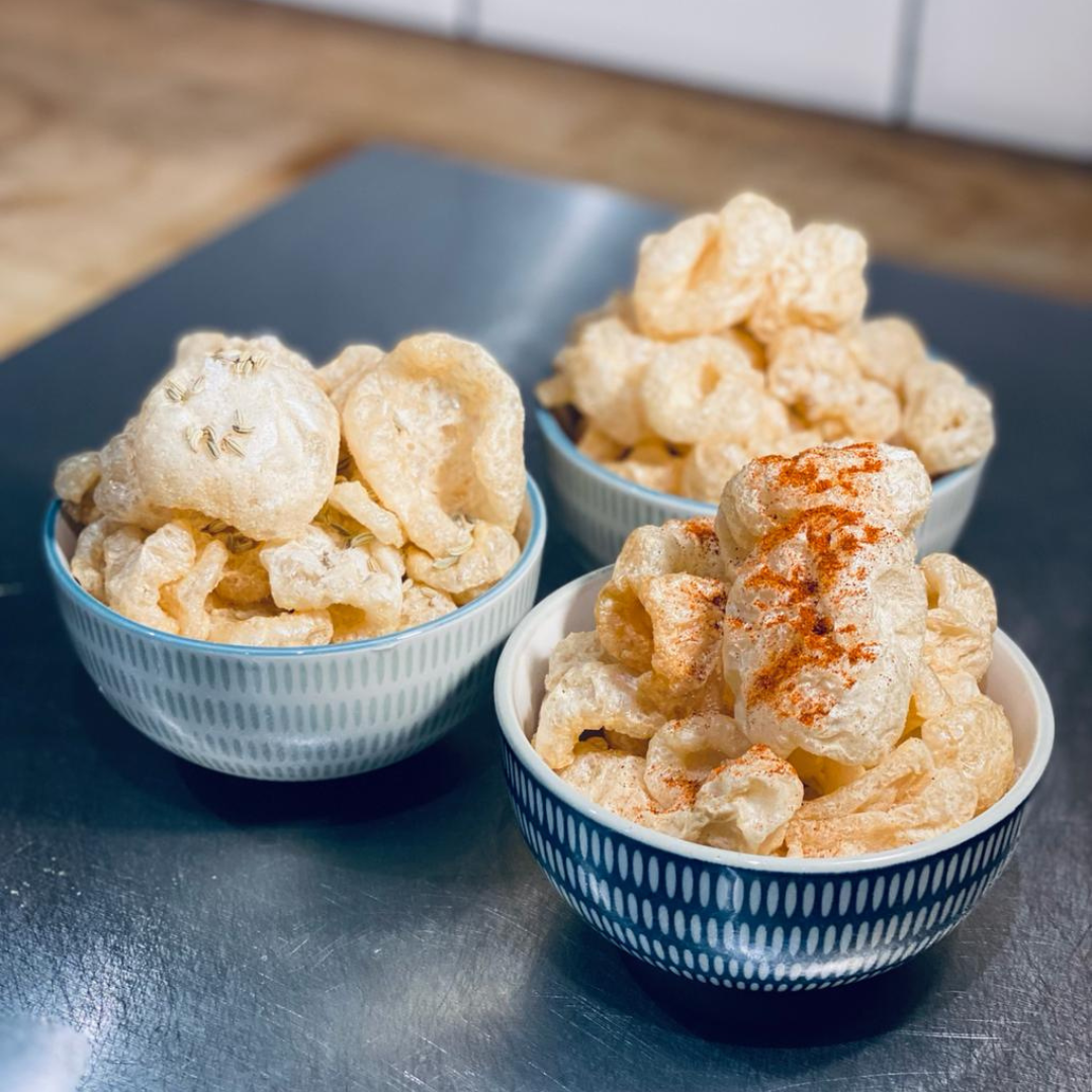 3 bowls of Made For Drink's crunchy Iberian Pork Chicharrónes. - one plain, one topped with a sprinkling of herbs, and another topped with dusting of smoked paprika.